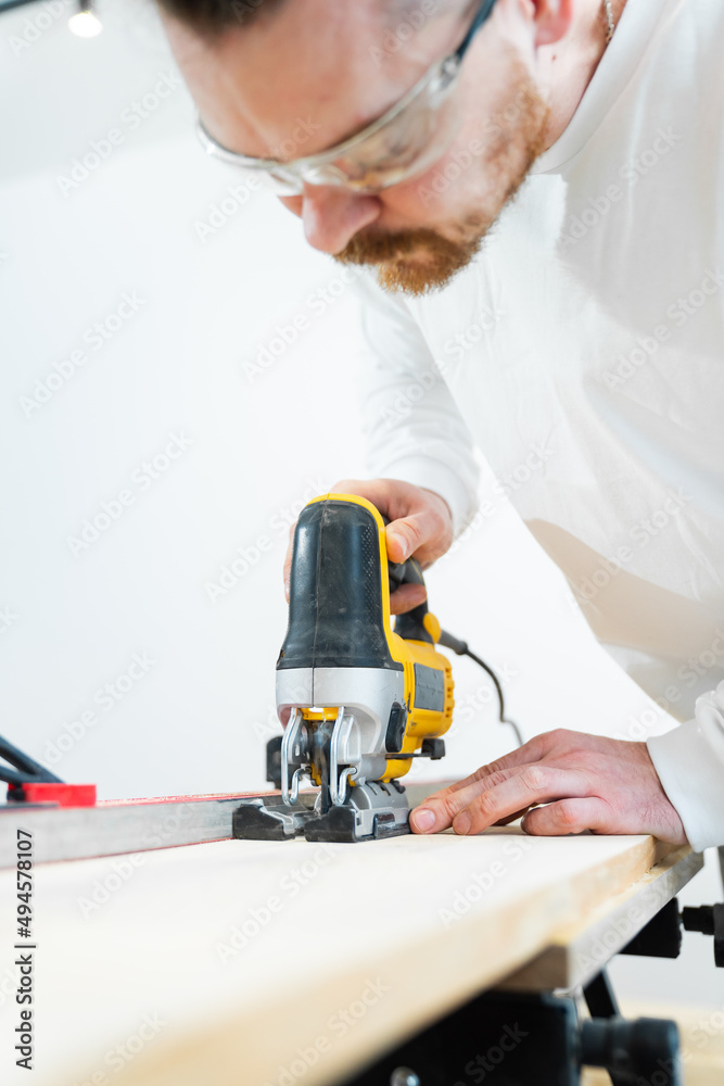 carpenter in protective glasses cuts wood with electric jigsaw