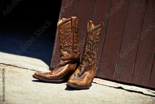 Worn in by hard work. Shot of a pair of cowboy boots outside a barn.
