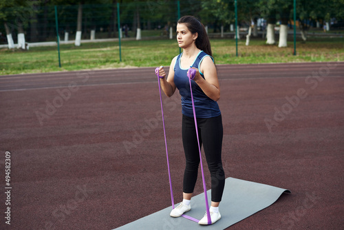 Young woman shakes muscles in her arms using an expander and fitness elastic bands. beautiful young sportswoman training with stretching band