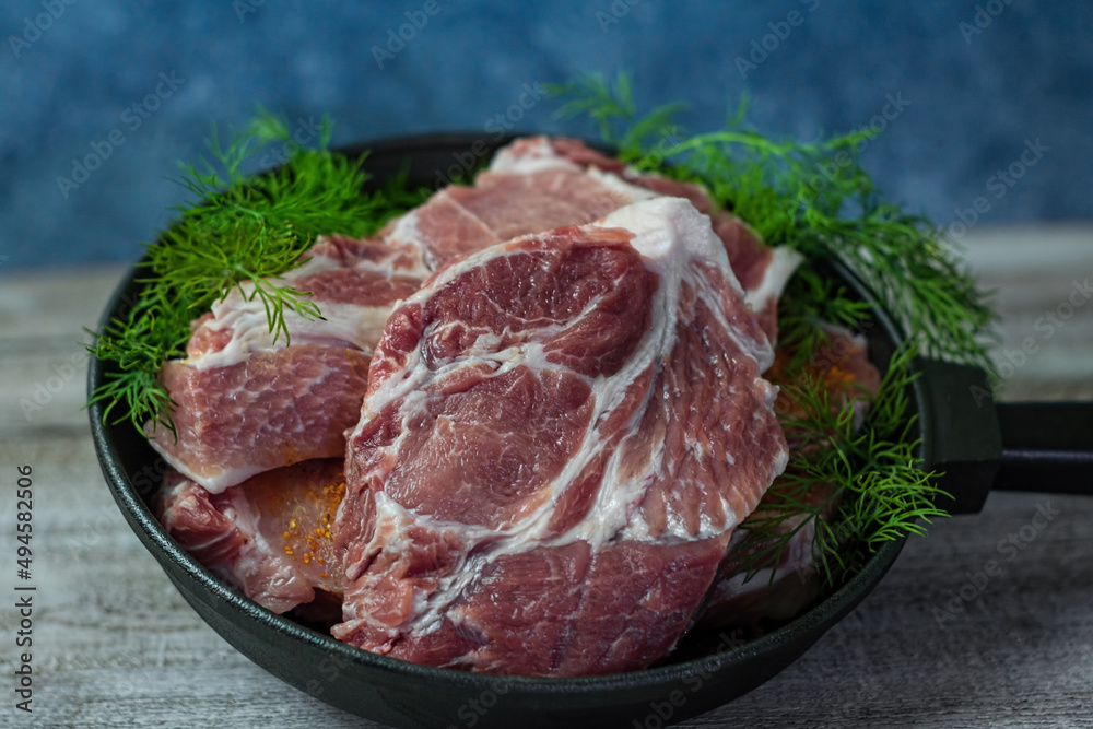 Close-up photo of cuts of meat with dill in a steak pan on wooden table with blue background