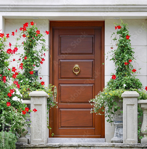 Elegant wooden front door surrounded by planters with red amaryllis flowers