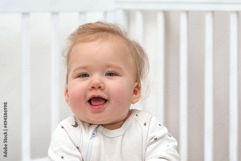 Close up portrait of a smiling baby sitting in a white crib