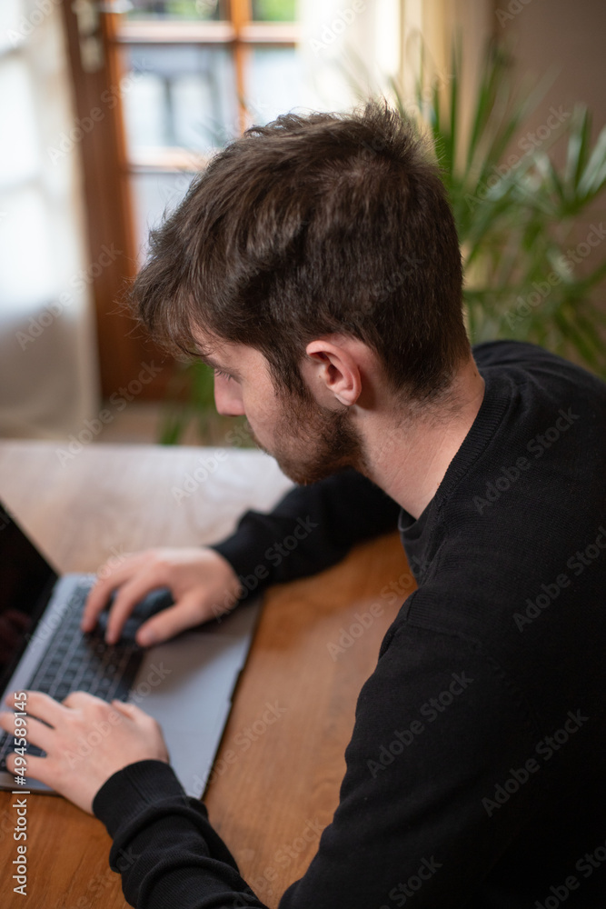 Jeune homme travaillant avec son ordinateur portable dans son salon, à la maison Jeune homme travaillant avec son ordinateur portable dans son salon, à la maison