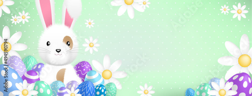 a cute white rabbit behind colored eggs and flowers on a green background