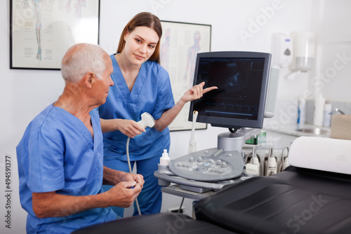 Portrait of young positive friendly technician showing new ultrasound scan to doctor in clinic