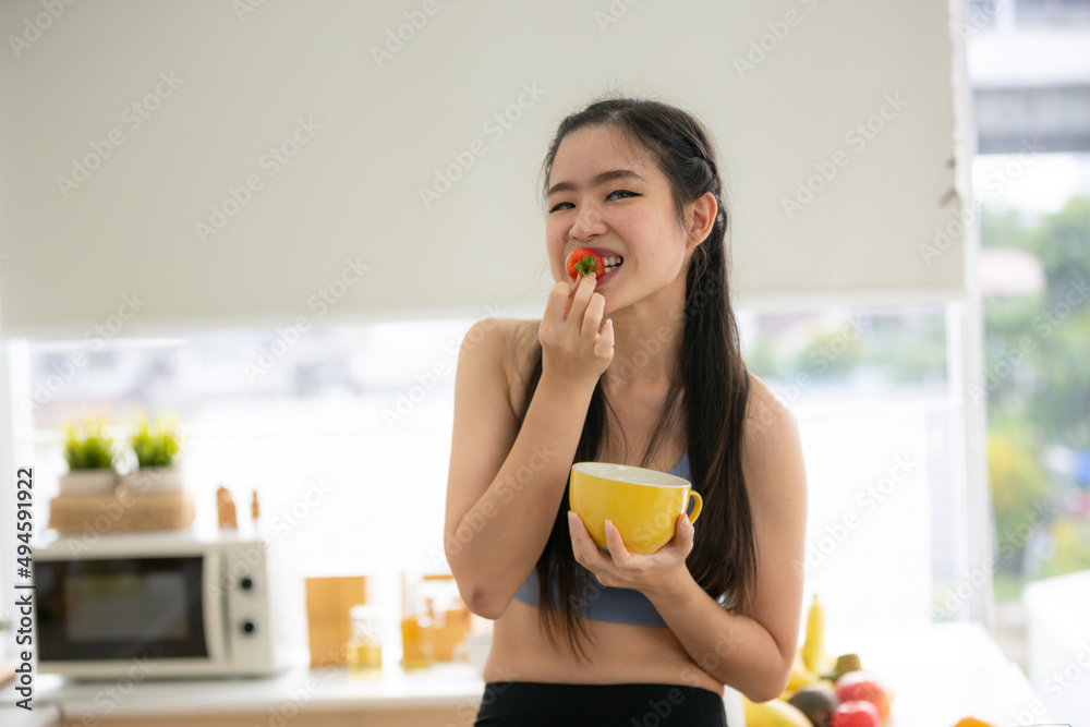 young Asian woman cooking vegetable healthy food and eating or drinking in home kitchen