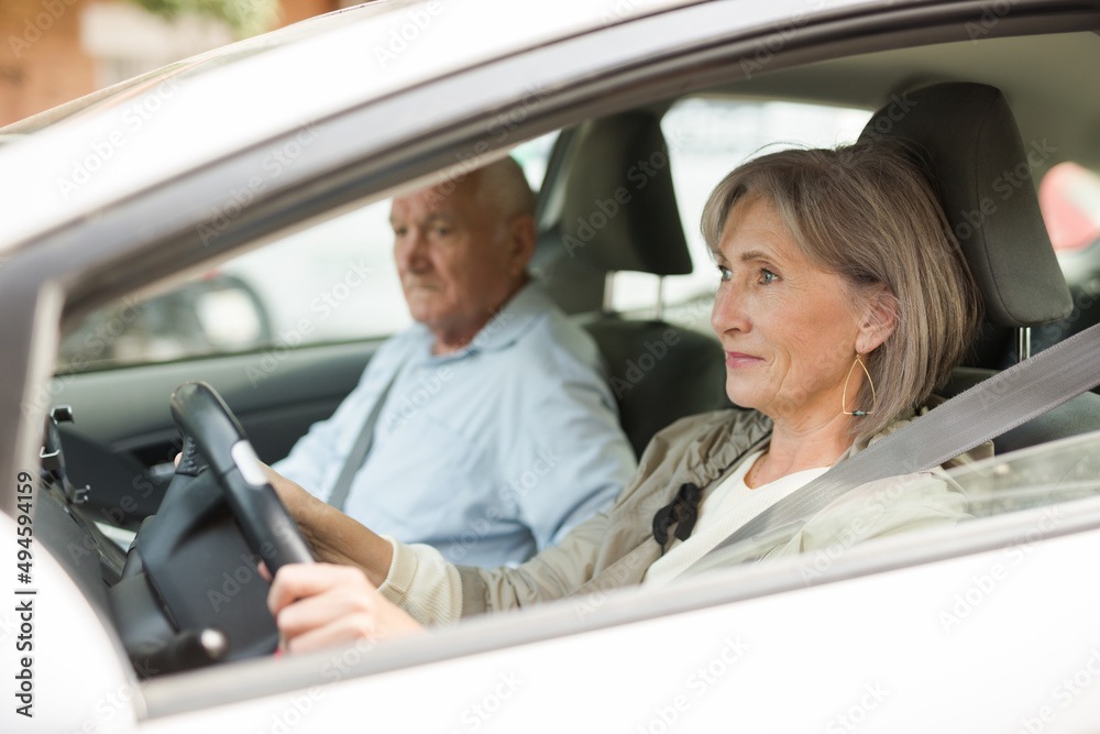 Elderly married couple driving a car in the city. Woman driving a car