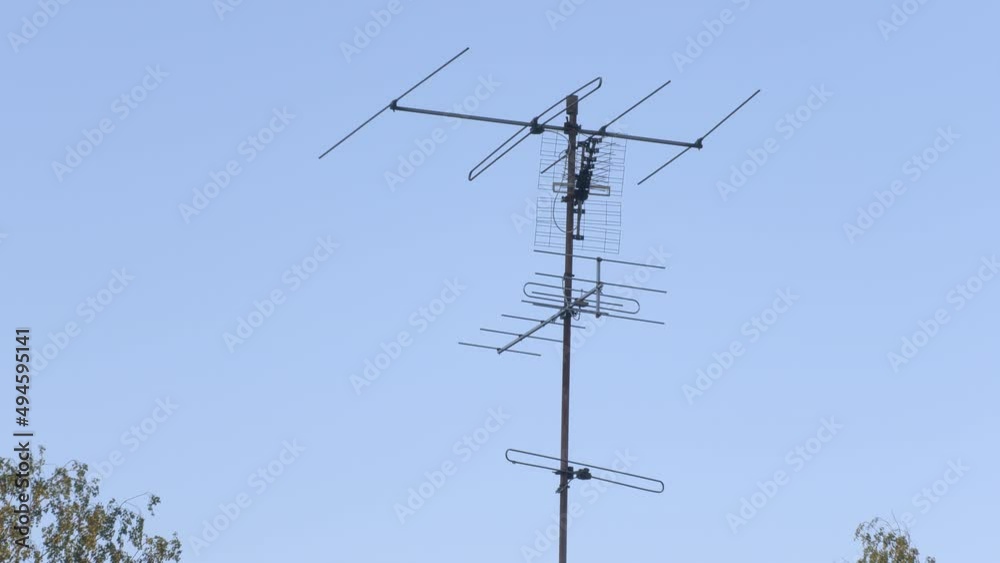 Beautiful shot of antennas on a roof with blue sky and trees in the background. Different antennas used for televisions. Camera slowly zooming in. Beautiful shot of antennas on a roof with blue sky and trees in the background. Different antennas used for televisions. Camera slowly zooming in.
