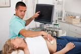 Young man sonographer using ultrasonography machine checking female patient in hospital diagnostic room