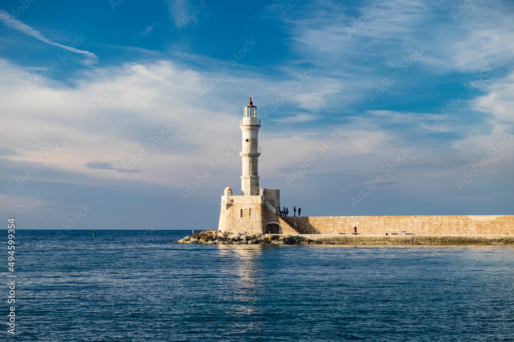 White stone lighthouse in the small marine bay of the old town on the mediterranean island in the evening sun