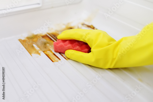 Person in protective gloves is cleaning of refrigerator from mold. Household chores. Cleaning services.