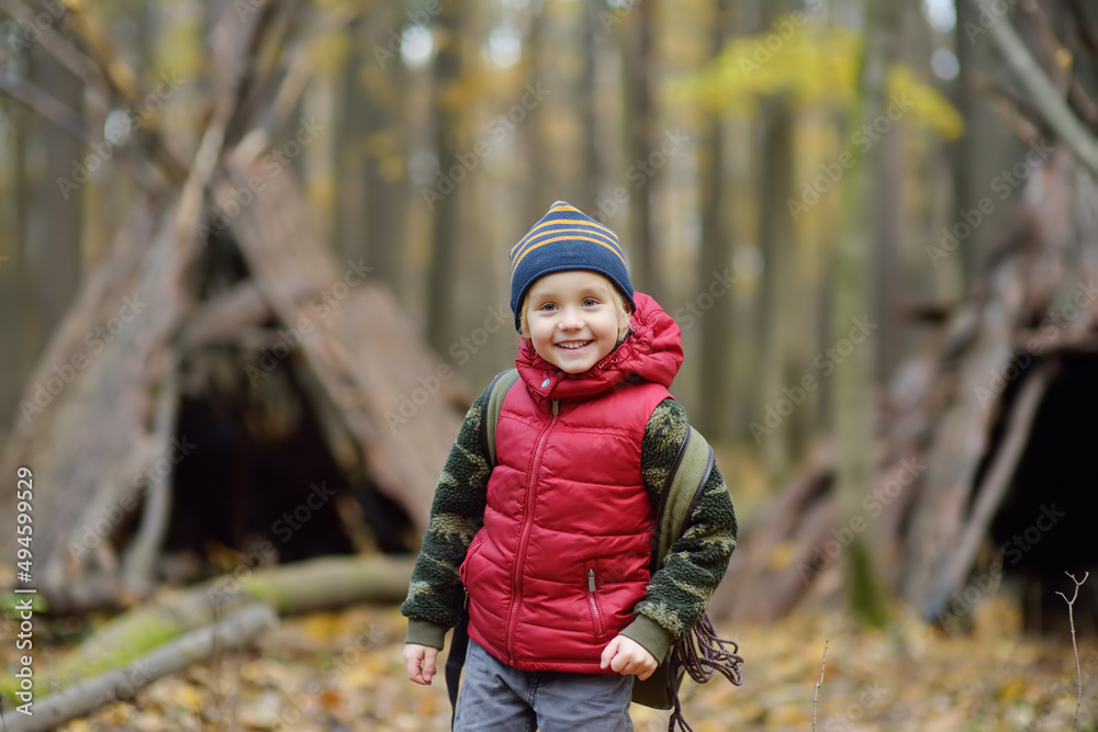 Little boy scout during hiking in autumn forest. Behind the child is teepee hut. Adventure, scouting and hiking tourism for kids. Little boy scout during hiking in autumn forest. Behind the child is teepee hut. Adventure, scouting and hiking tourism for kids.