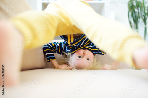 Little boy is standing on own head on sofa at home. Bored lonely child. Difficulties of family with preschool children during working at home. Baby having fun and standing upside down.