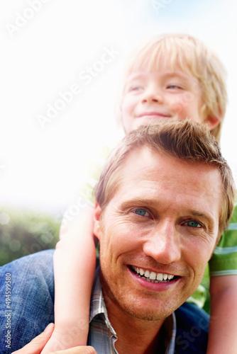 Smiling mature man giving his son piggyback ride. Closeup portrait of a smiling mature man giving his son piggyback ride. © Stigur/peopleimages.com