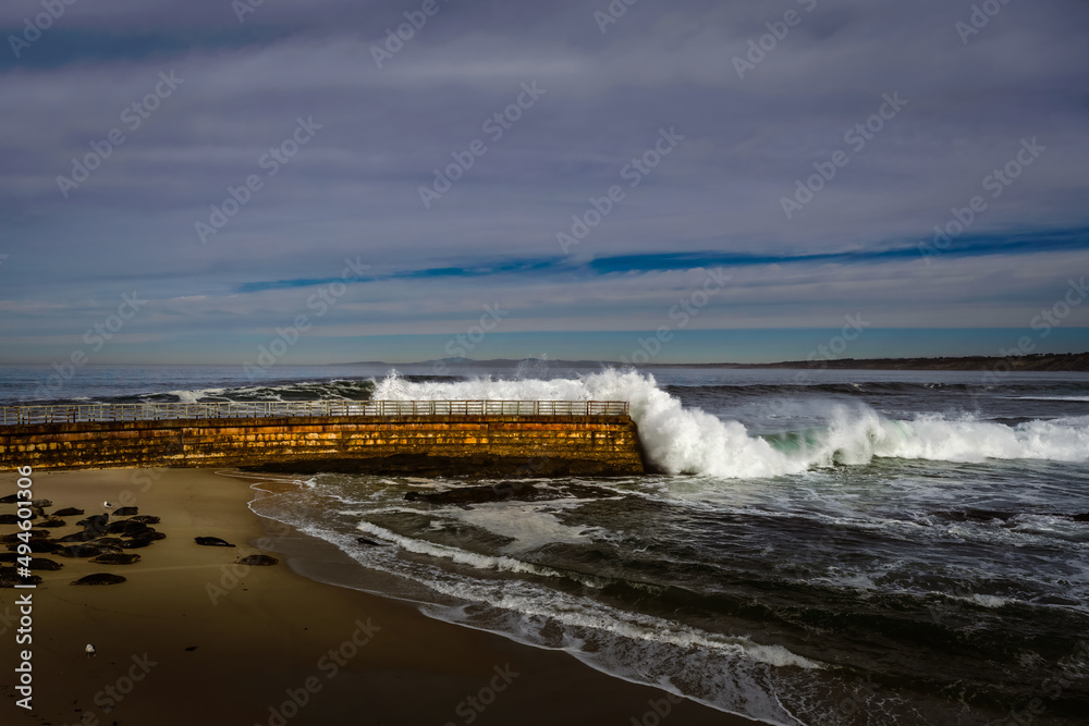 2022-03-23 THE CHILDRENS POOL AND WALK WAY IN LA JOLLA CALIFORNIA WITH WAVES CRASHING ON THE BARRIER AND SEALS ON THE SAND WITH A CLOUDY SKY 2022-03-23 THE CHILDRENS POOL AND WALK WAY IN LA JOLLA CALIFORNIA WITH WAVES CRASHING ON THE BARRIER AND SEALS ON THE SAND WITH A CLOUDY SKY