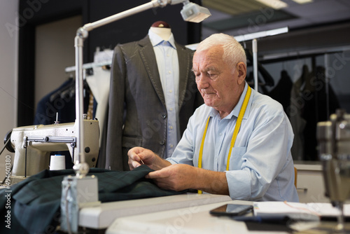 Elderly tailor sews lapel to a jacket in his workshop