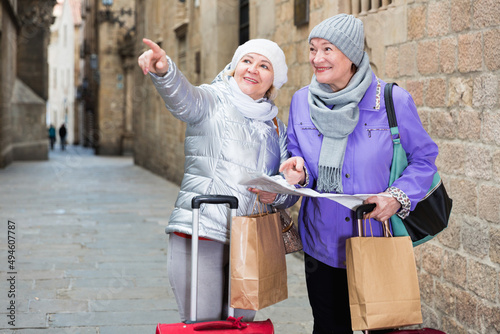 Two positive elderly women tourists with city guide walking on street