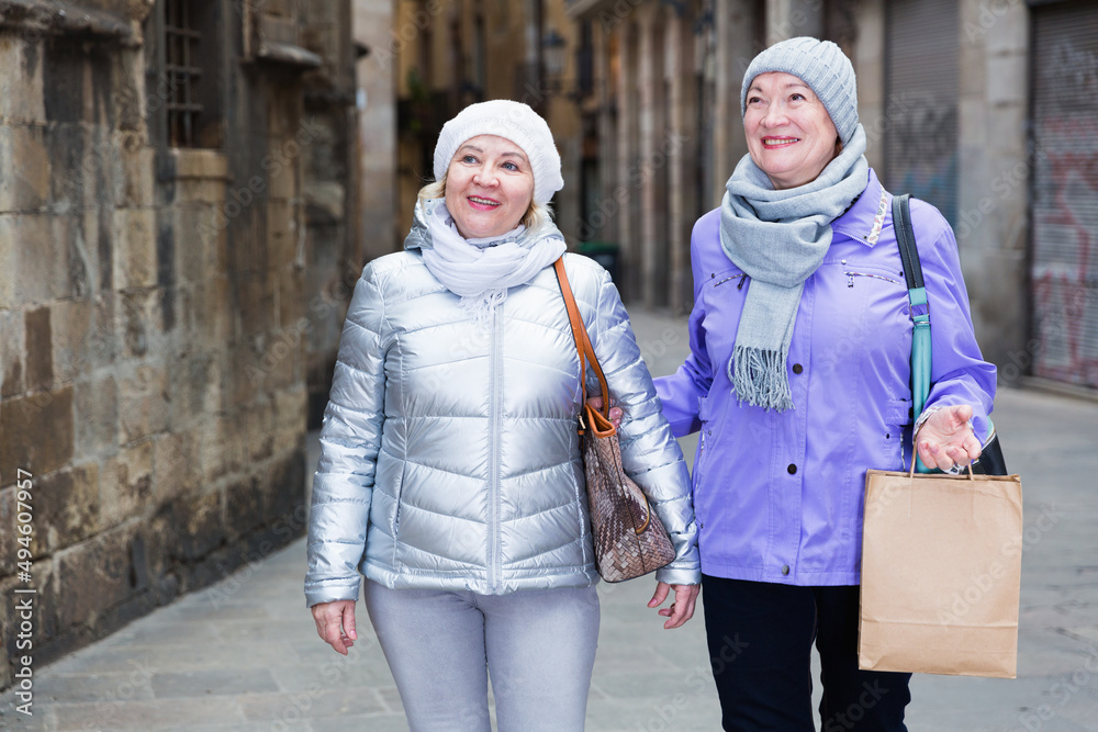 Senior woman with female friend walking together along autumn city streets