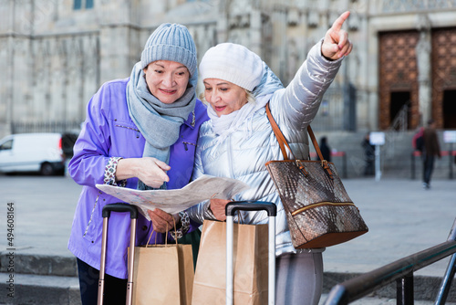 Senior woman with female friend traveling together looking for destination with city map.