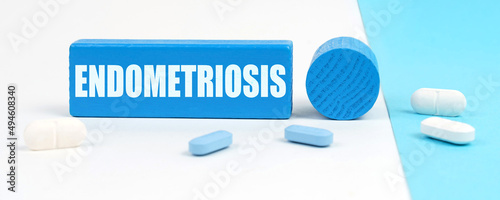 On a white and blue surface are pills, a pen and a wooden sign with the inscription - Endometriosis