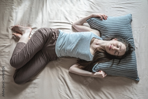Young happy woman is lying in bed in the morning with her eyes closed and waking up. Concept of healthy sleep, comfort and a pleasant start of new day. Top view