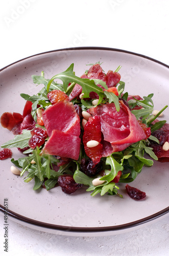 Salad with smoked duck breast, arugula, dried cranberry and pine nuts served on the ceramic plate. Exquisite appetizer