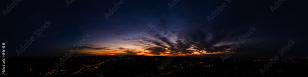 Obraz premium Dark wispy clouds in a deep blue sky in the afterglow of an golden sunset above the street lights aerial panoramic