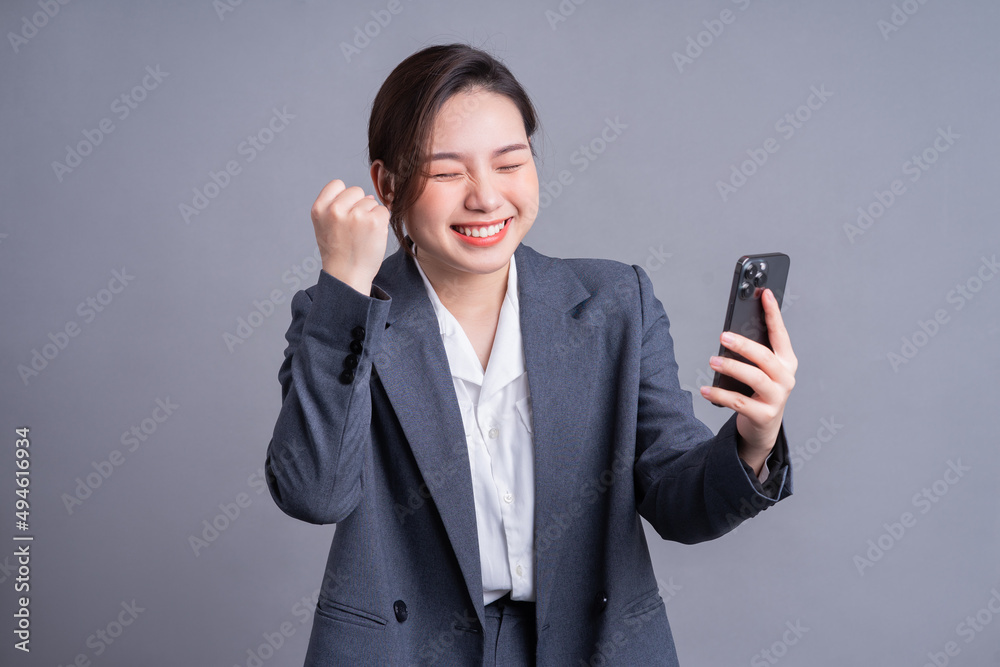 Young Asian businesswoman holding smartphone on gray background Young Asian businesswoman holding smartphone on gray background