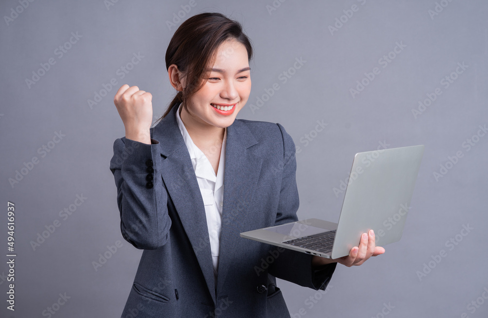 Young Asian business woman wearing suit and using laptop on gray baclground