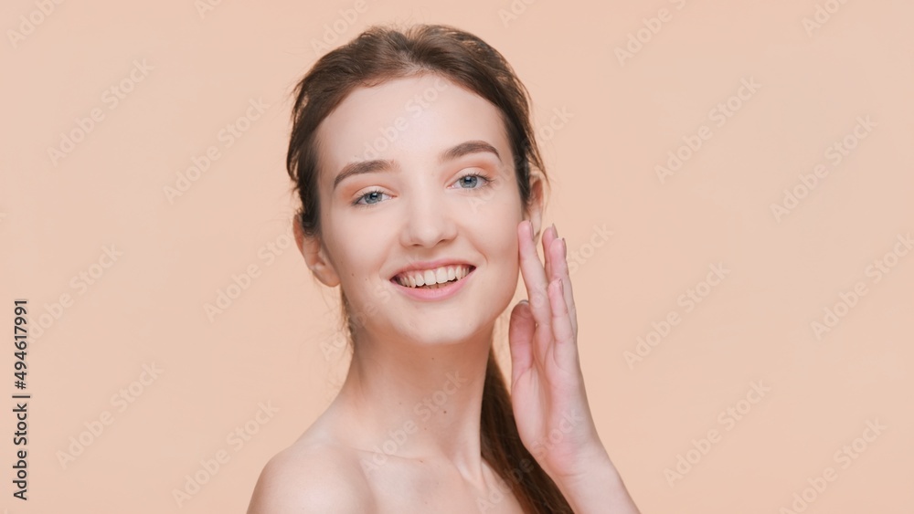 Young attractive brown-haired woman with perfect skin touches her face and looks at camera on dark beige background Young attractive brown-haired woman with perfect skin touches her face and looks at camera on dark beige background