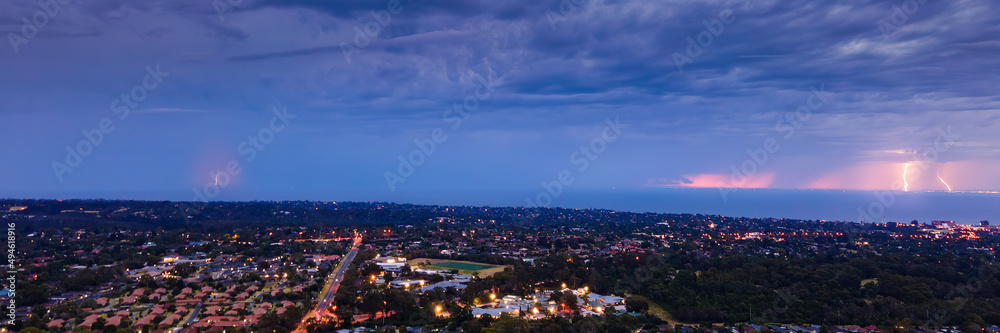 Distant lightning strikes across Port Philip Bay seascape filled with stormy clouds and street lights aerial panoramic