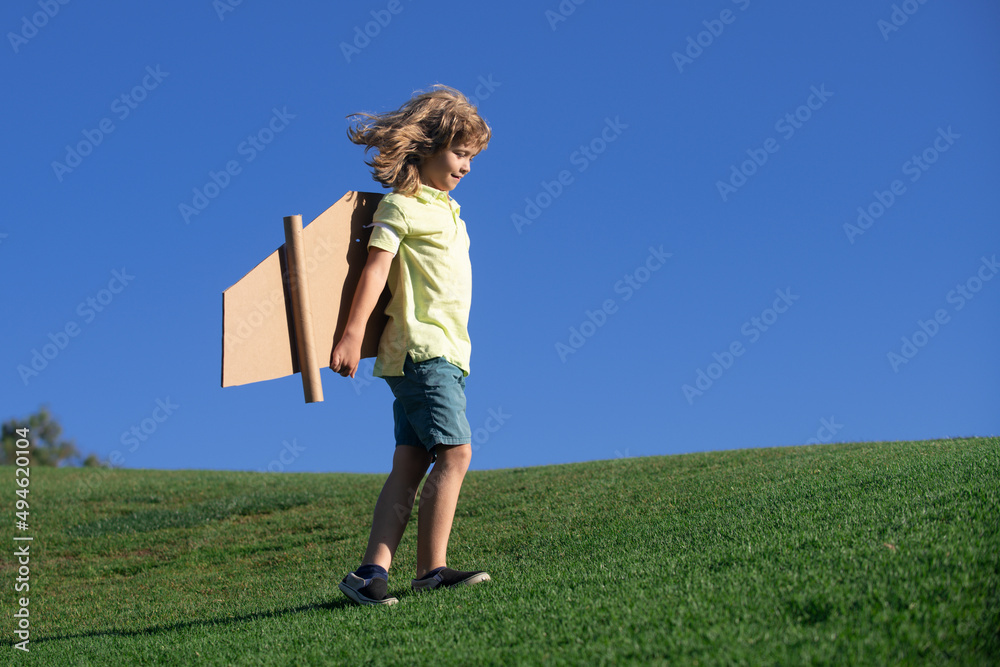 Portrait of cute blond child play pilot with handmade craft paper plane wings. Kids dreaming, success, creative and startup concept. Copy space for text.