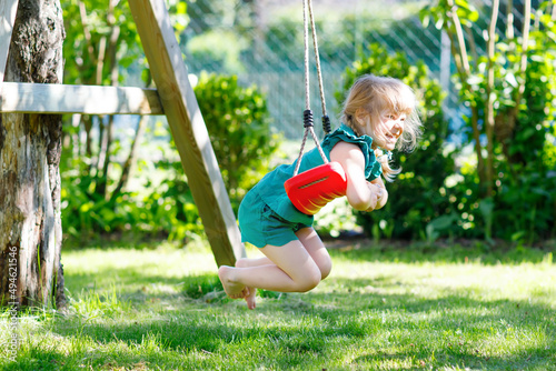 Happy little preschool girl having fun on swing in domestic garden. Healthy toddler child swinging on sunny summer day. Children activity outdoor, active smiling kid laughing photo