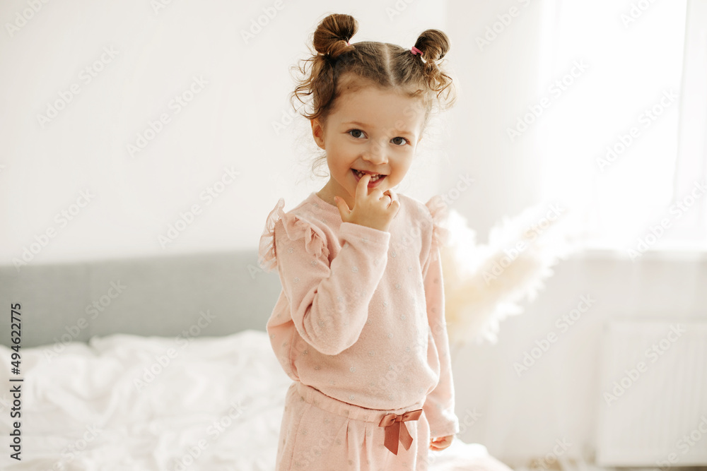 Portrait of a happy girl standing on the bed in the bedroom in the morning after waking up