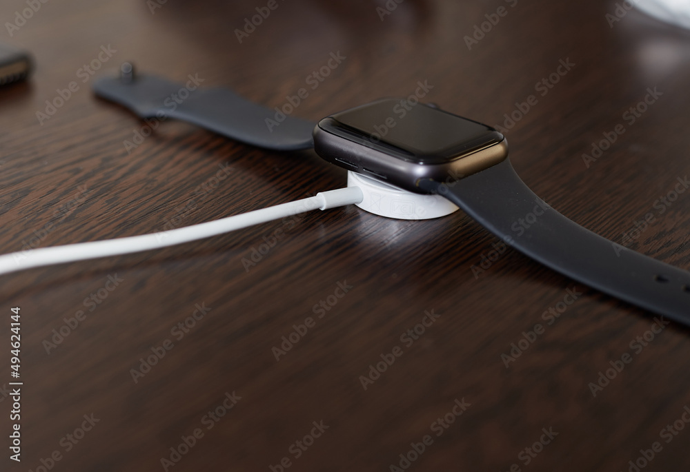 The black watch is on charge, wireless charging of the wristwatch gadget - obrazy, fototapety, plakaty 