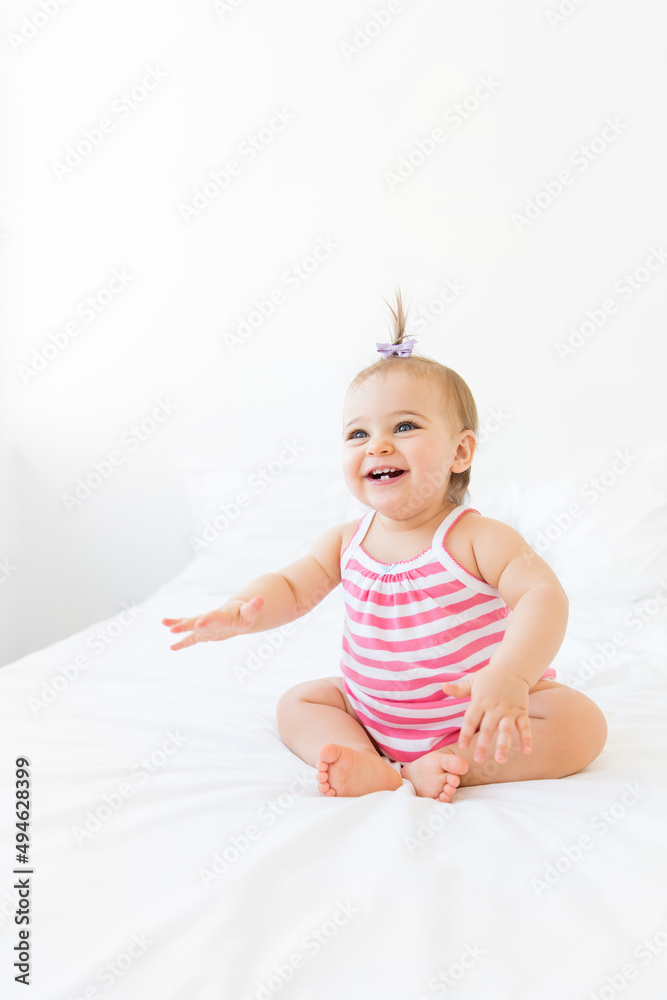 Happy baby girl with pigtail sitting on white bed Happy baby girl with pigtail sitting on white bed
