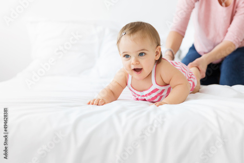 Baby lying on white bed with mother pulling on her feet