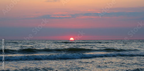 The sun is half covered by the horizon. Beautiful sunset on the sea. Selective focus.