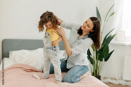 A young mother helps her little daughter to change clothes. Taking care of children, help, motherhood