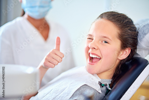 In the hot seat. Portrait of a young girl sitting in a dentists chair giving a thumbs up.