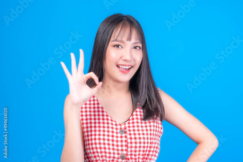 Beautiful beauty Asian woman cute girl with bangs hair style in red dress shows ok sign with hands smile face enjoy and happy isolated on blue background - lifestyle Asian girl Concept