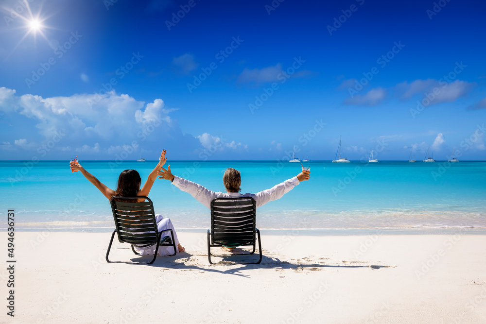 Back view of a happy vacation couple sitting on a tropical beach in the Caribbean and enjoying their summer holidays