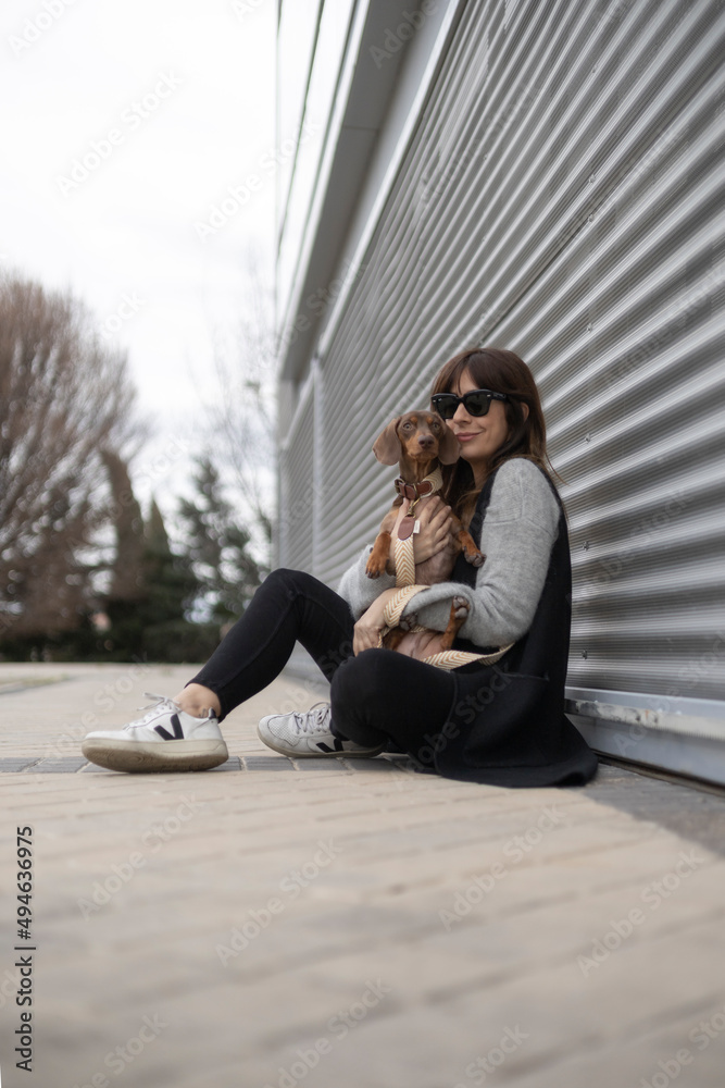 Naklejka premium Girl petting small Dachshund dog in the street