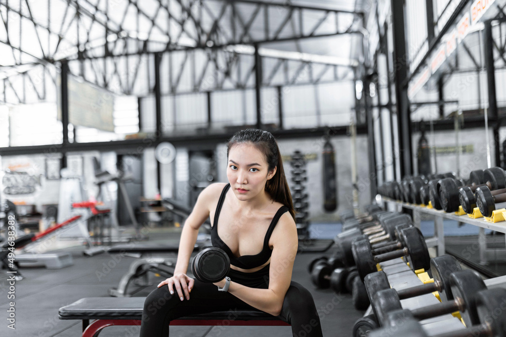 exercise concept The strong built woman in black sport top and pants and a smartwatch working out with the dumbbell by doing concentraction curl on her left arm