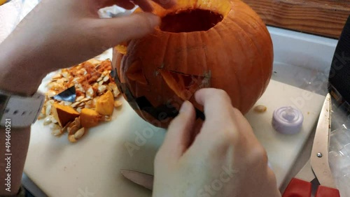 Pumking being carved to make a jack-o'-lantern for Halloween. Female and kids hand remove pieces of the pumking with the shape of the eyes. Some scissors are used to remove pieces and fibre. photo