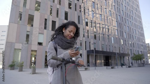 Happy smiling Business Woman walking using smart phone financial center urban city street with e-scooter. Young people ride eco transport healthy lifestyle with modern architecture background.