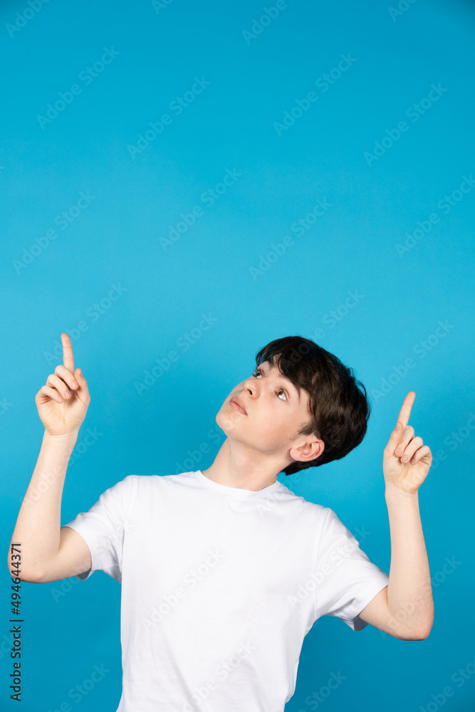 Cute teenager boy pointing up to blue copy space Cute teenager boy pointing up to blue copy space