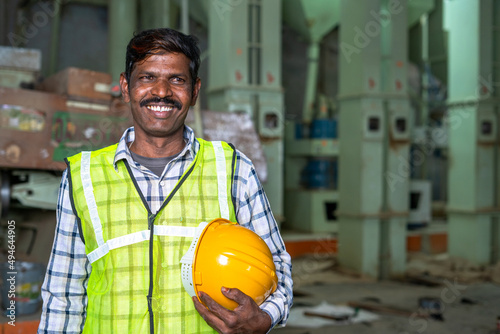 Portrait of happy smiling industrial worer with safety helmet in hand looking at with copy space - concept of safety measures, skilled labour and workforce.