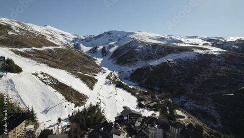 Flyover Sierra Nevada town towards Snowy mountain with ski resort tracks, Andalusia