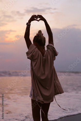 A young beautiful woman on the shore of the ocean at sunset enjoys freedom, place, time. View from the back. flowing clothes. #494647103